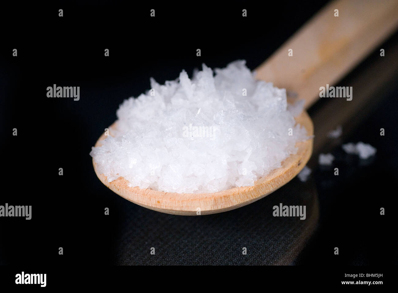 Natürliche Meersalz Flocken auf einem Holzlöffel mit schwarzem Hintergrund Stockfoto