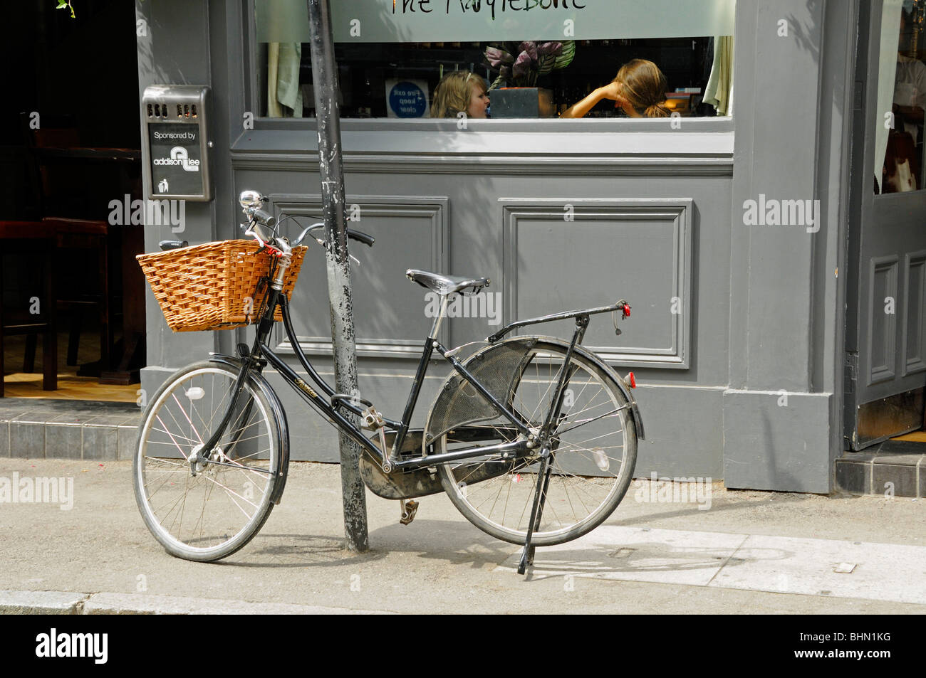 Damenrad mit Korb angekettet, um außerhalb der Marylebone Bar London England UK buchen Stockfoto