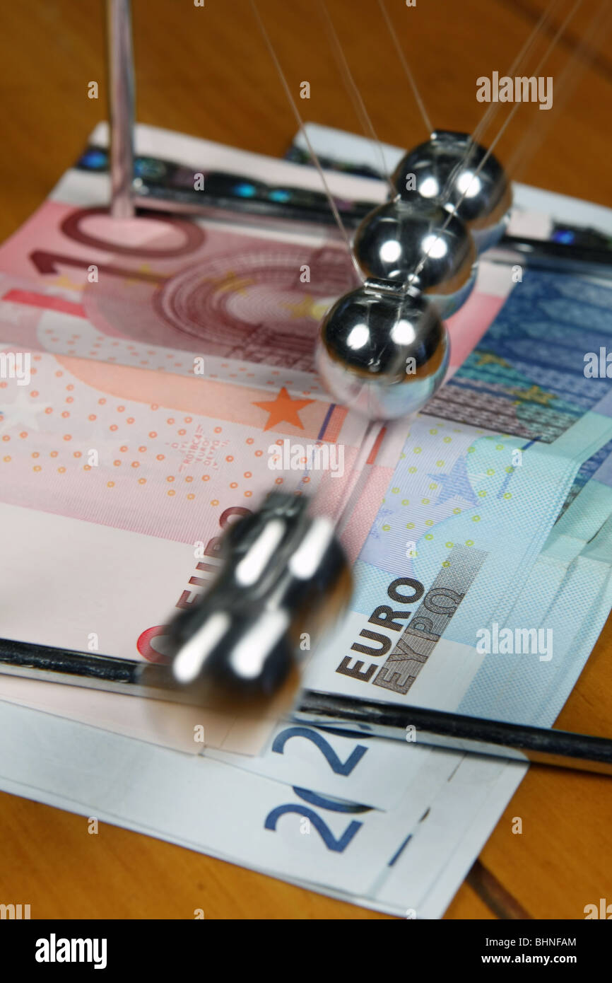 5 Metallkugeln schwingen auf einem Gestell auf einige 20 und 10-Euro-Banknoten Stockfoto