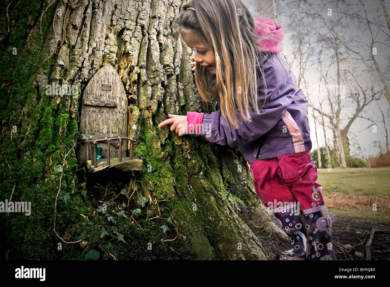 Ein junges Mädchen entdeckt eine Fee Tür in einem magischen Wald Baum Stockfoto