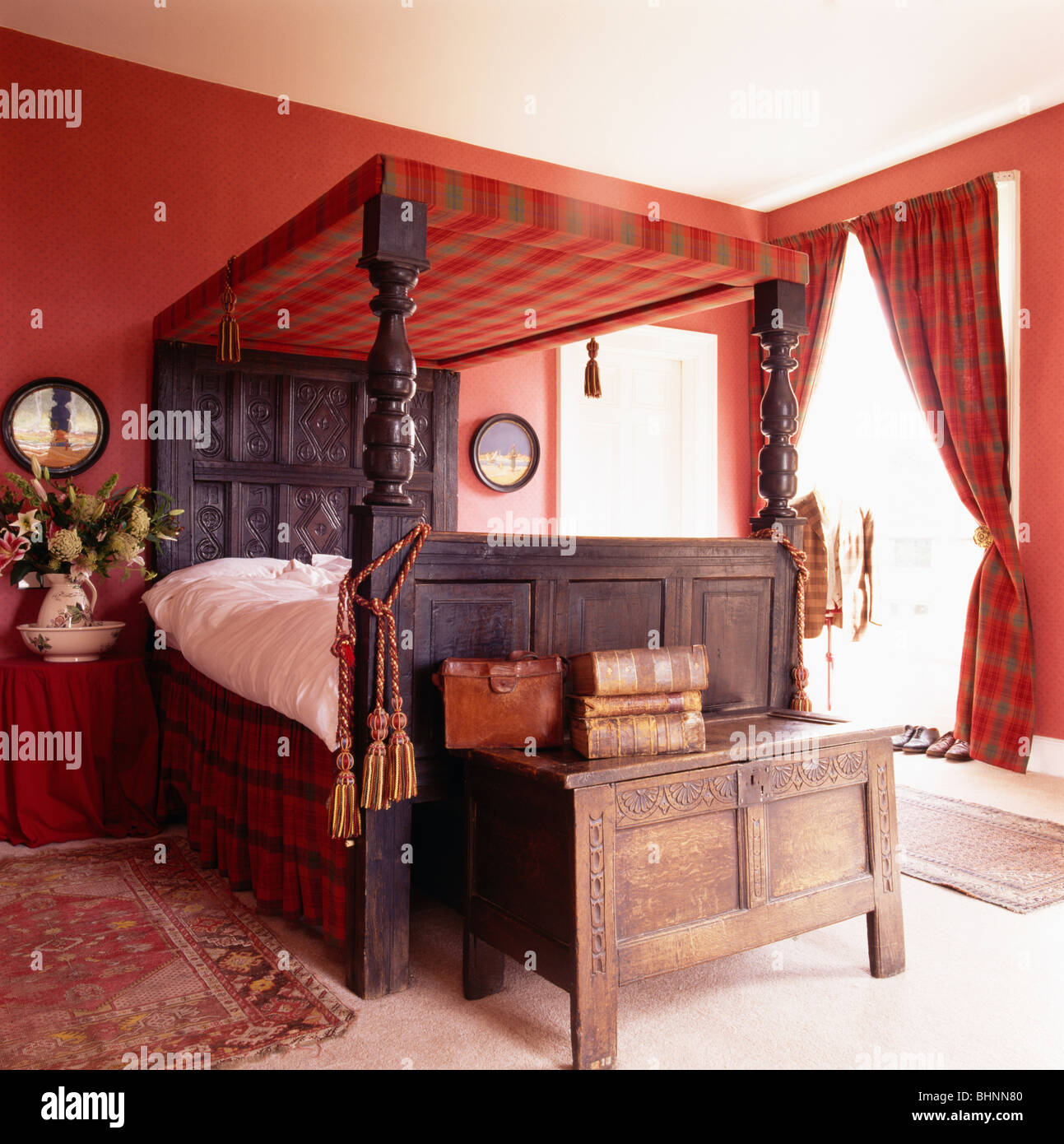 Antik geschnitzte hölzerne Truhe unter Himmelbett im roten Schlafzimmer mit  rot karierten Vorhänge Stockfotografie - Alamy