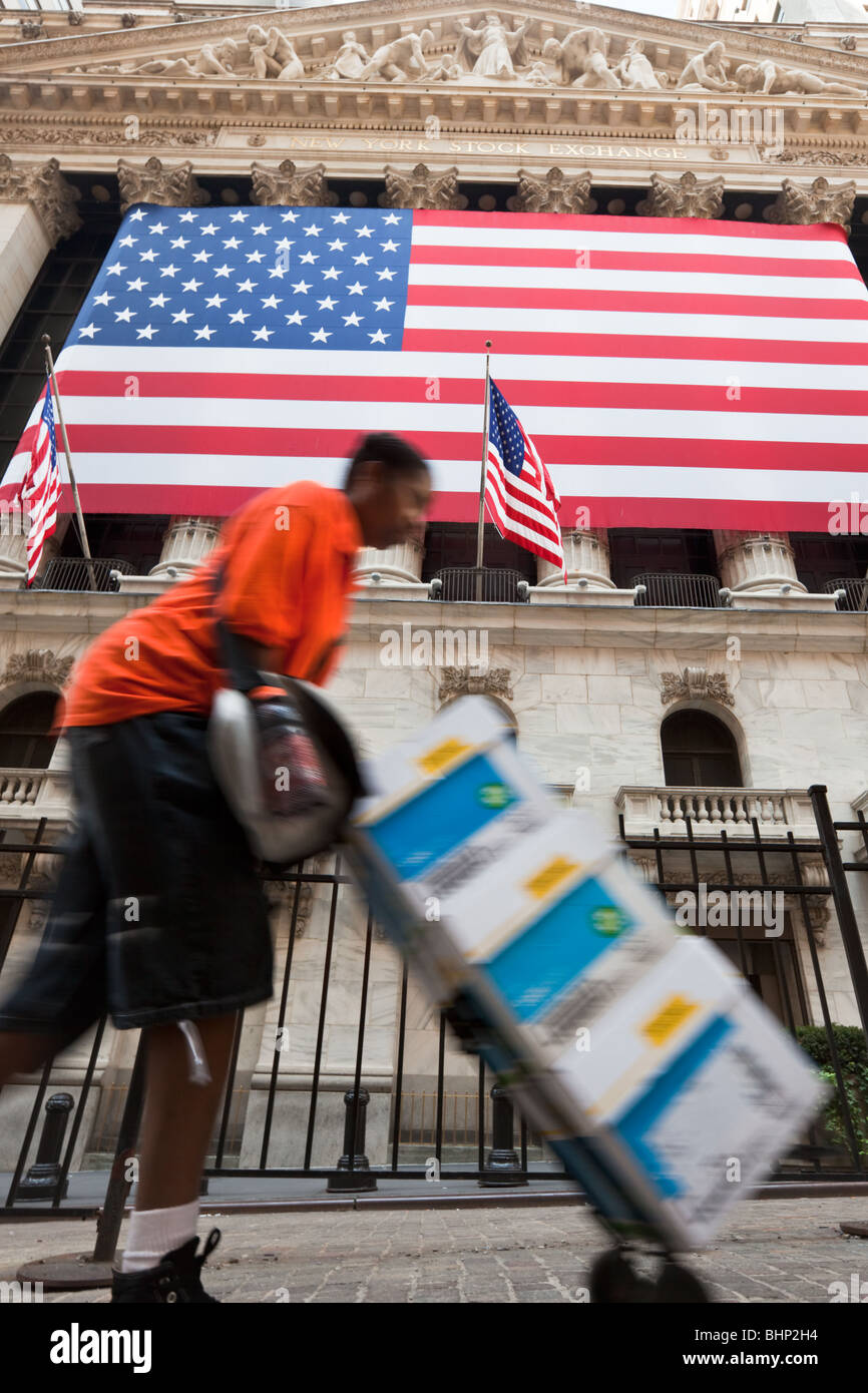 New York Stock Exchange mit afroamerikanischen vorbei schieben Kisten auf Wagen in Bewegung verwischen mit US-Flagge. Stockfoto