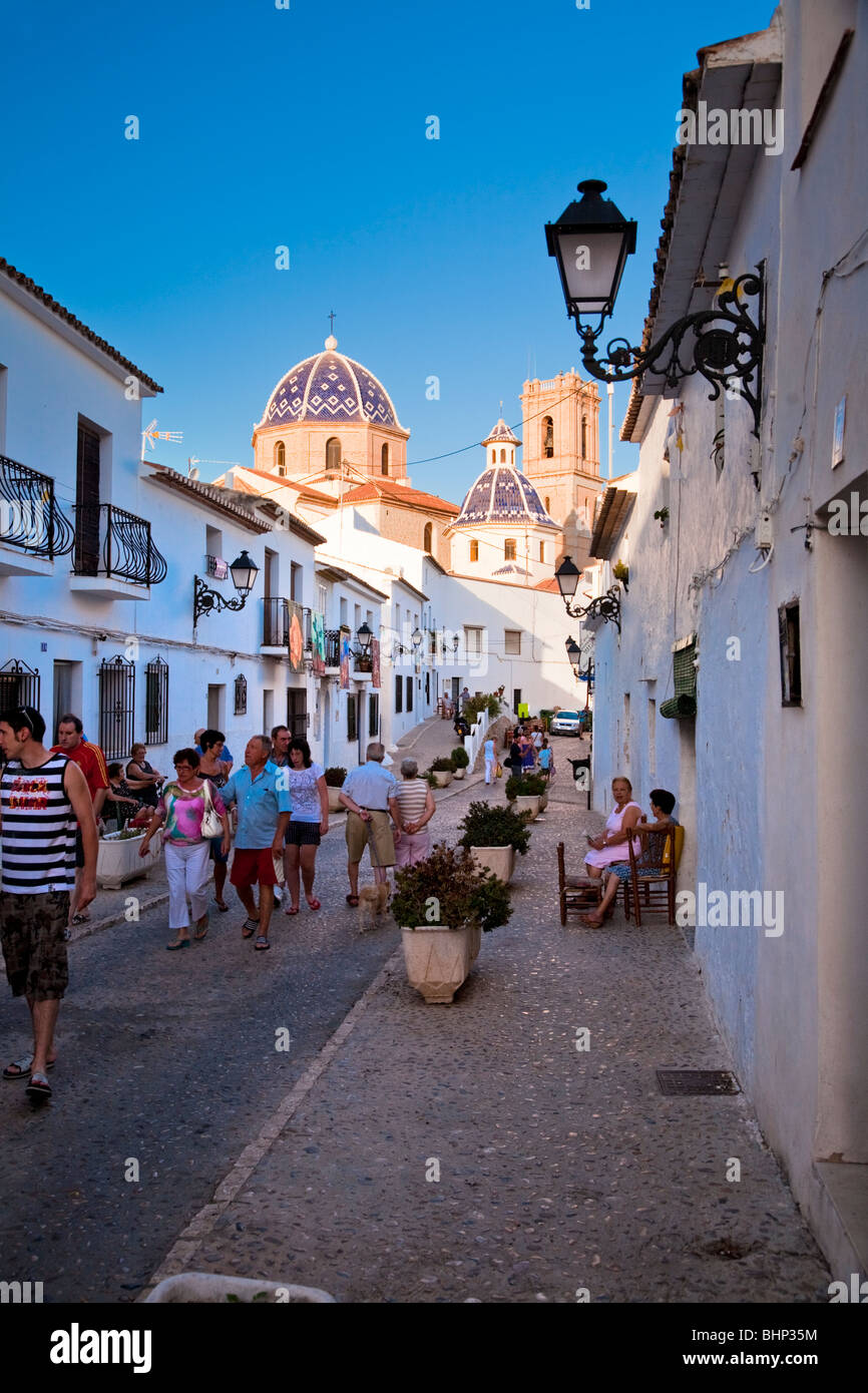 Menschen auf Straße, [Calle San Miguel] Altea, Alicante, Spanien. Mit Kirche "Virgen del Consuelo" im Hintergrund Stockfoto