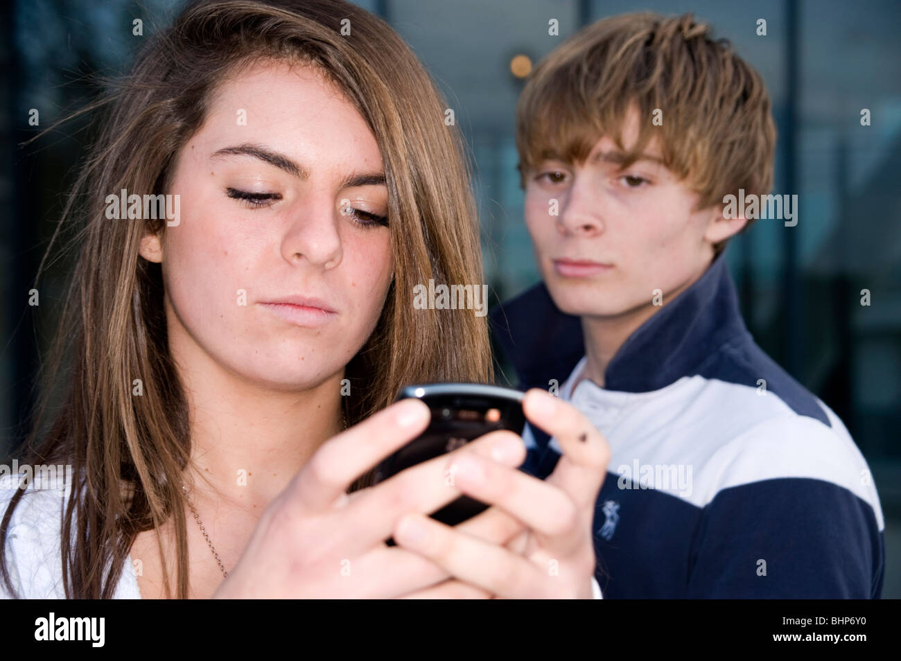 Teenager-Mädchen auf eine mobile Blick auf einen Text mit einem Teenager im Hintergrund suchen eifersüchtig Stockfoto