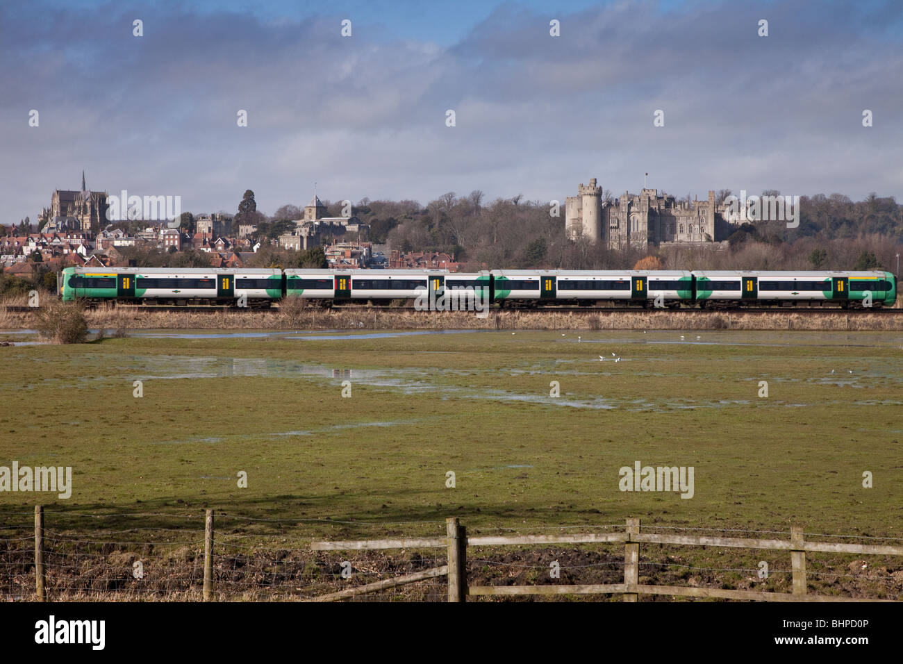 Ein Zug vorbei Arundel Town in Sussex mit der Burg und die Kathedrale im Hintergrund und einem aufgeweichten Feld sichtbar vorne Stockfoto