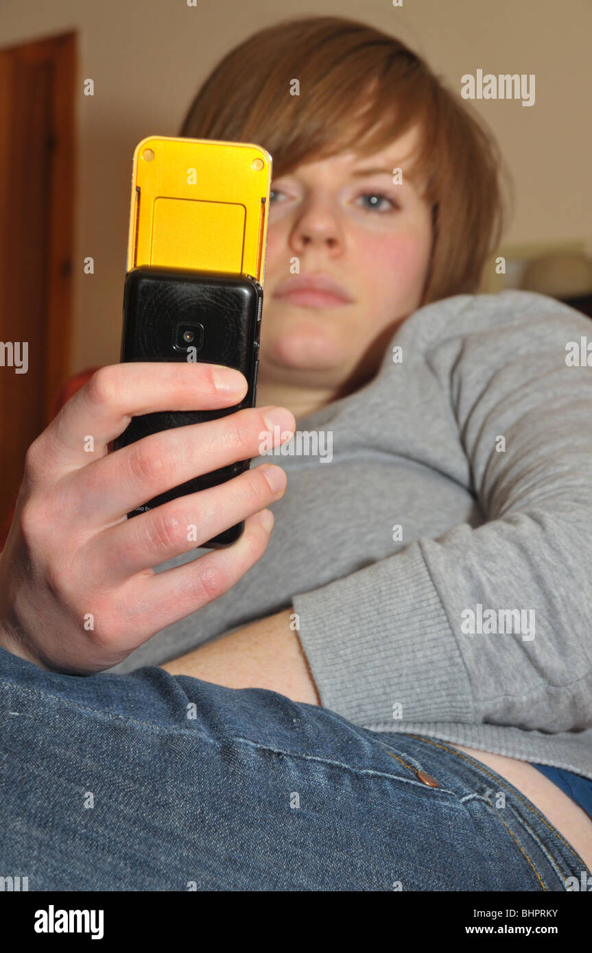 Eine junge Frau liest ihre SMS-Nachrichten auf ihr Handy beim Faulenzen auf dem Sofa. Stockfoto