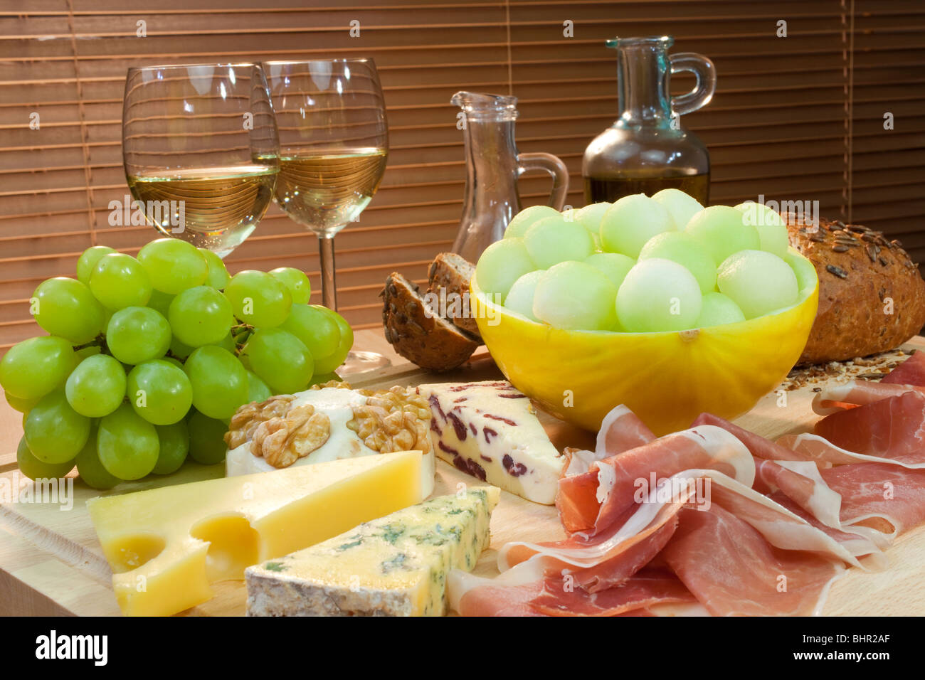 Eine Platte mit mediterranen Speisen wie Käse, Trauben, Wein, Brot, Parmaschinken, Melone, Olivenöl und Balsamico-Essig. Stockfoto