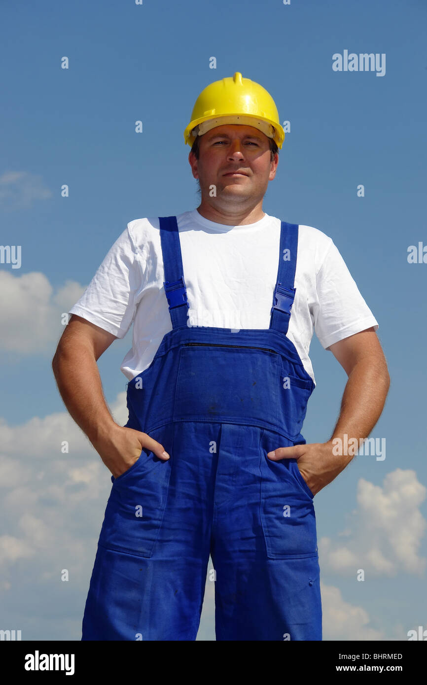 Zuversichtlich Bauarbeiter tragen gelbe Helm und blauen Sprunganzug posiert über blauen Himmel Stockfoto