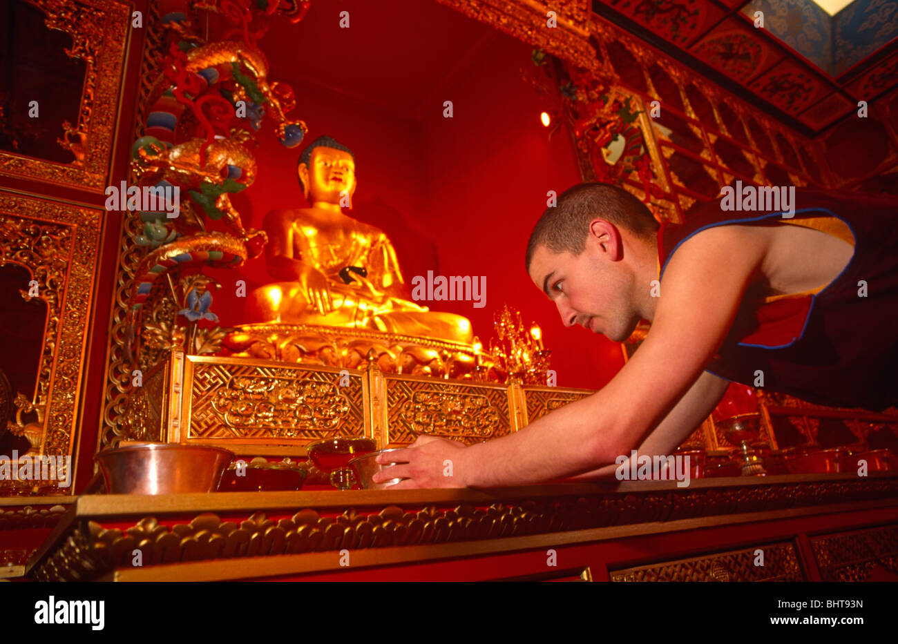 ein junge Anhänger des tibetischen Buddhismus passt eine Gebet Schüssel vor ein Bildnis des Buddha in Klosters Kagyu Samye Ling. Stockfoto
