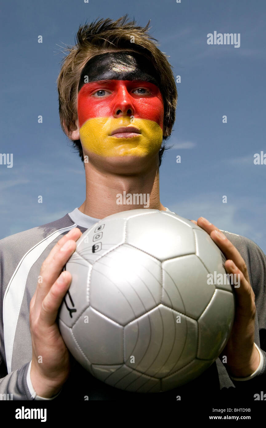 eine ernste aussehende deutsche Fußball-Anhänger mit der deutschen Flagge  gemalt auf seinem Gesicht ein Fußball hochhalten Stockfotografie - Alamy