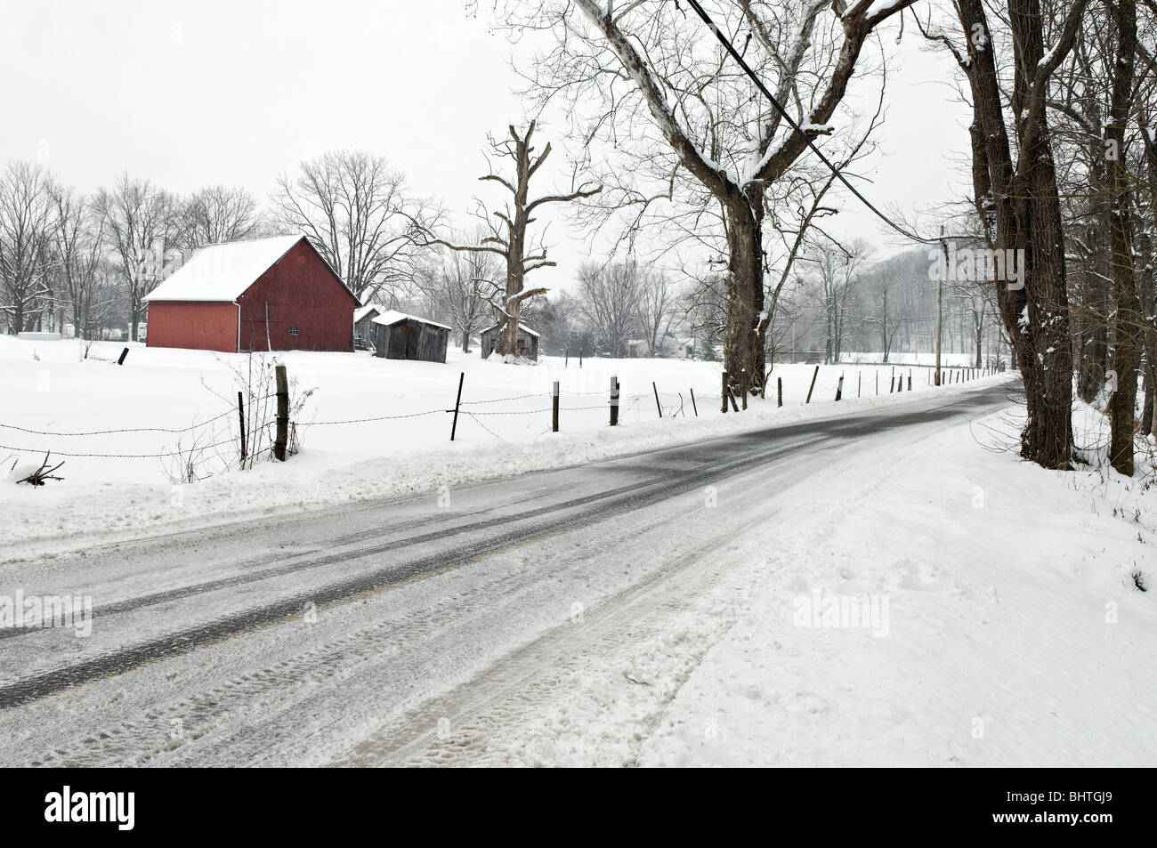 Rote Scheune, Zaun und Grafschaft-Straße im Schnee in Floyd County, Indiana Stockfoto