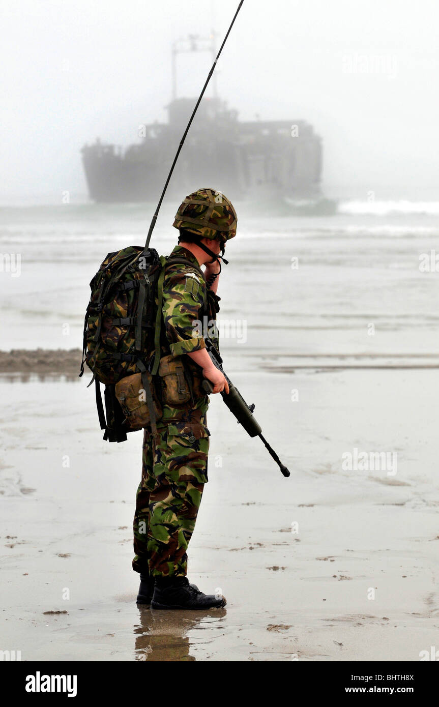 Kommunikation-Marine mit Landungsboote hinter Soldat mit Kommunikation Radio während einem Strand landen, UK Stockfoto