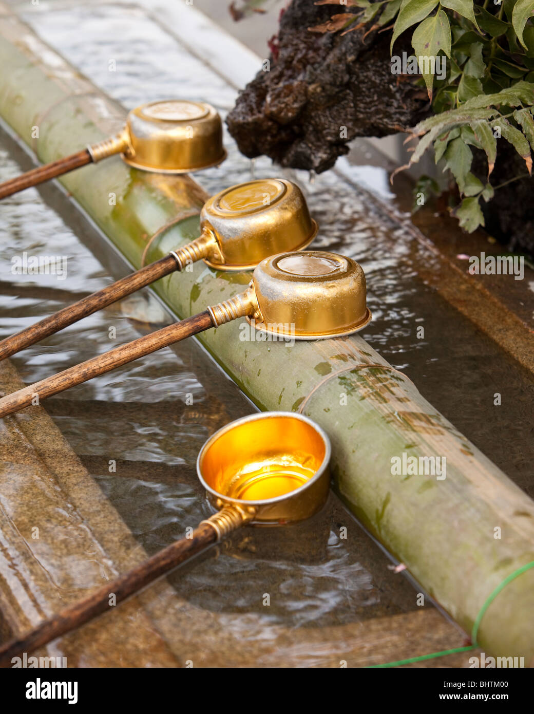 Vier metallische Schöpfkellen voll Wasser warten darauf, in ein Reinigungsritual verwendet werden. Stockfoto
