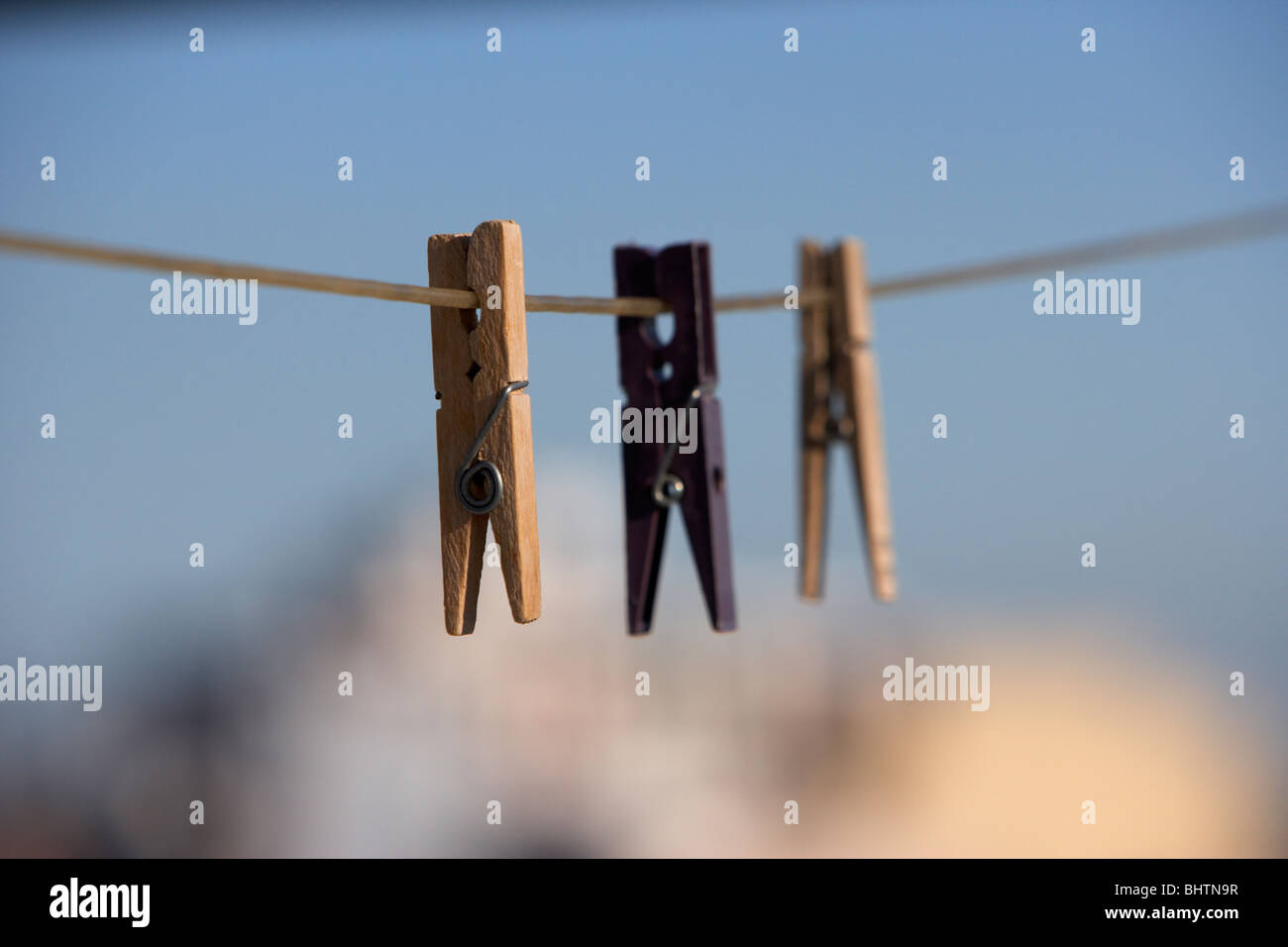 drei Wäscheklammern an einer Wäscheleine vor einem strahlend blauen Himmel über der Stadt hängen Stockfoto