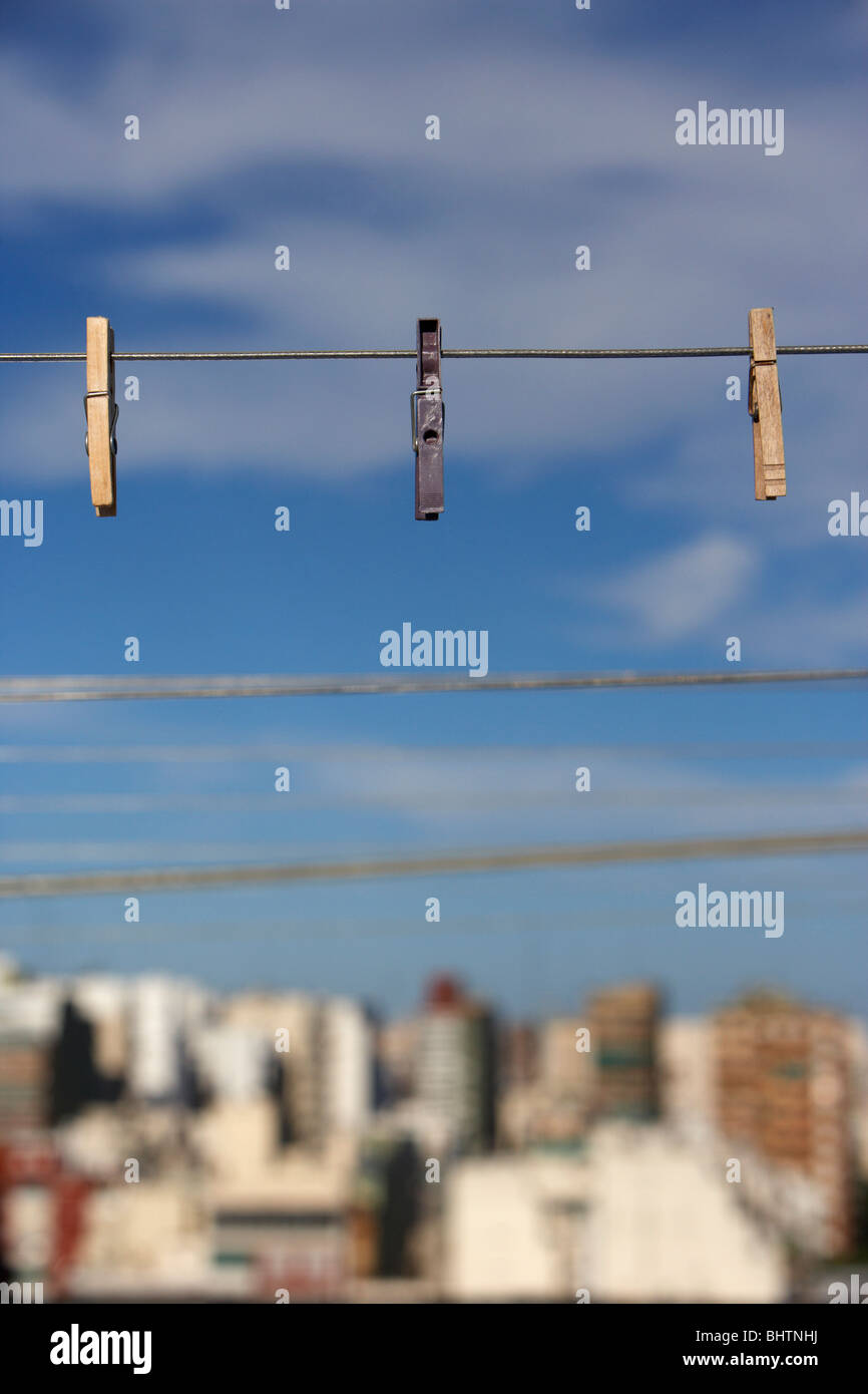 drei Wäscheklammern an einer Wäscheleine vor einem strahlend blauen Himmel über der Stadt hängen Stockfoto