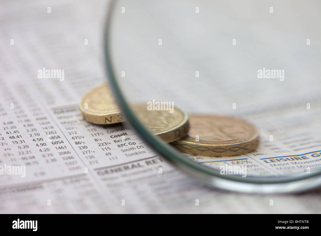 Makroaufnahme von 1- und 2-Pfund britische Münzen auf einer Zeitung Anzeige Aktien und Aktien Preise durch eine Lupe betrachtet. Stockfoto