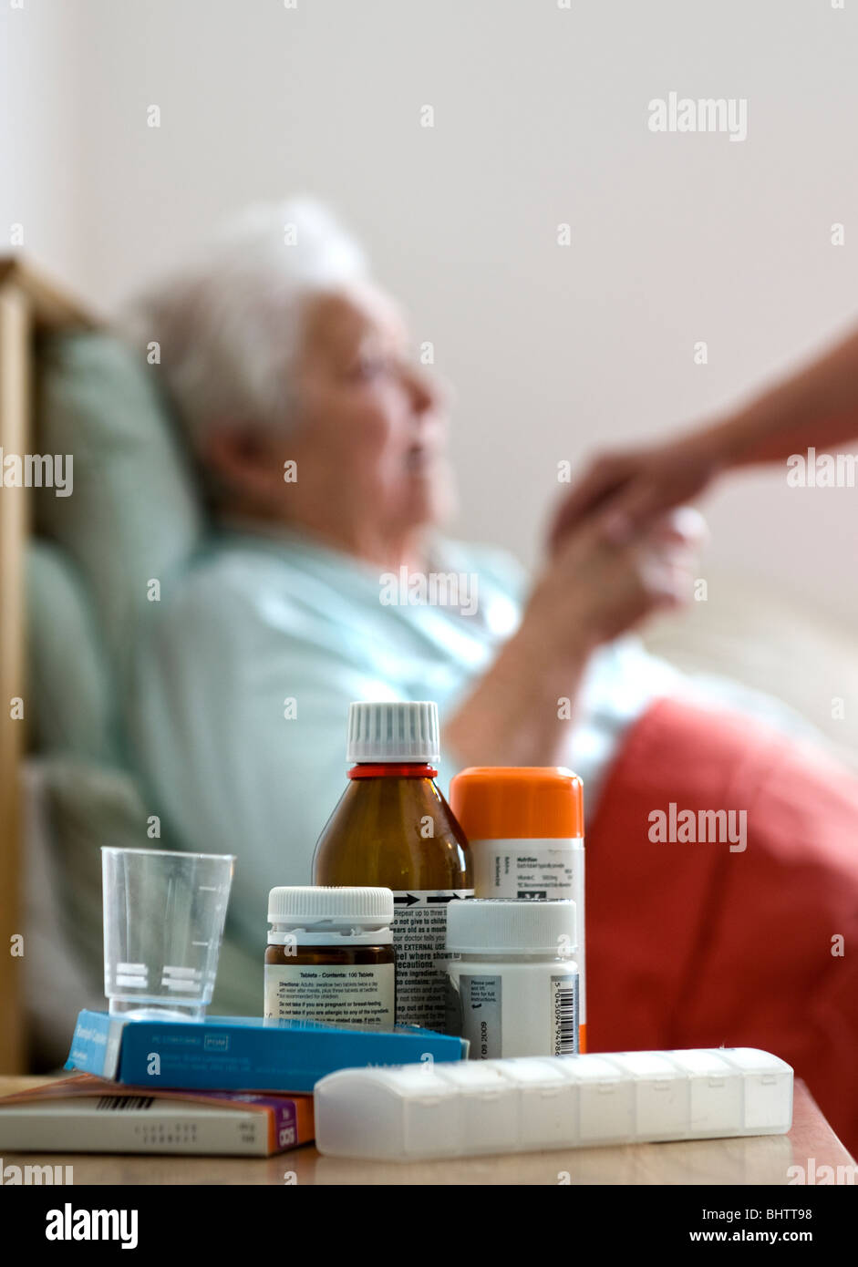CORONAVIRUS ältere Kovid-19-Seniorin im Pflegeschlafzimmer, im Bett mit beruhigender Pflegekranken-Besucherin, die ihre Hand hält, Medikamente im Vordergrund Stockfoto