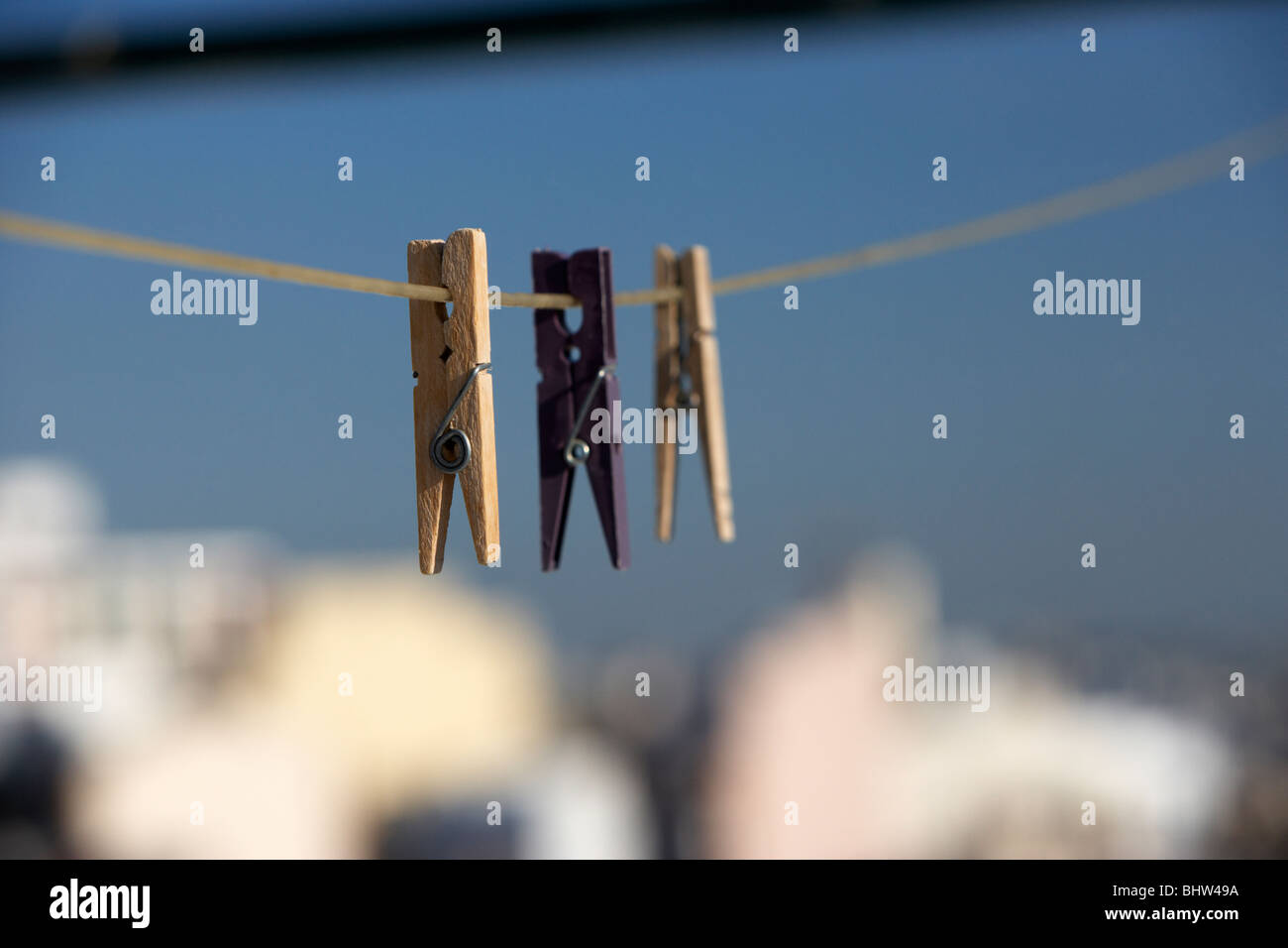 drei Wäscheklammern an einer Wäscheleine vor einem strahlend blauen Himmel über der Stadt hängen Stockfoto