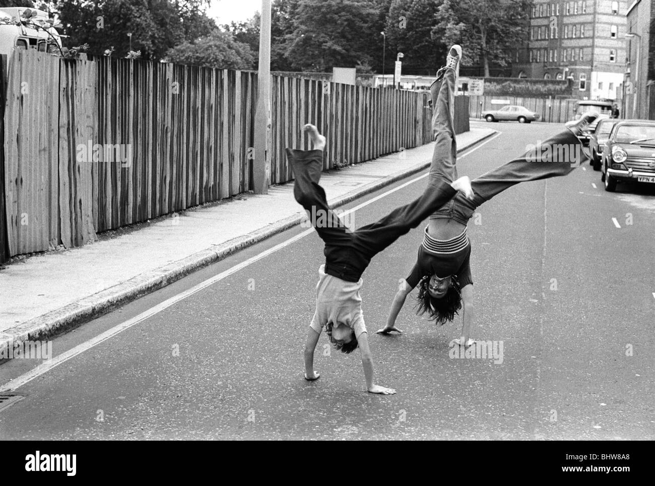 Teenager-Mädchen, die in der Oswin Street SE11 Elephant and Castle, South London UK 1975, auf Wagenrädern drehen. Im Hintergrund befindet sich das Rowton House, das später zum London Park Hotel wurde. Das Mädchen, das der Kamera am nächsten ist, hat keine Schuhe an, sie geht barfuß. HOMER SYKES Stockfoto