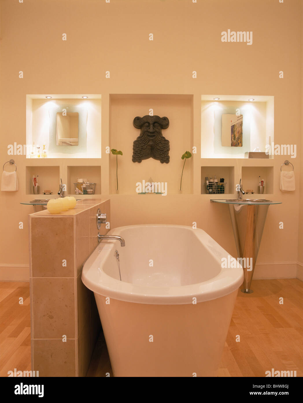 Freistehende Badewanne neben niedrigen geflieste Trennwand in modernes weißes Bad mit Spiegel in beleuchtete Nischen Stockfoto