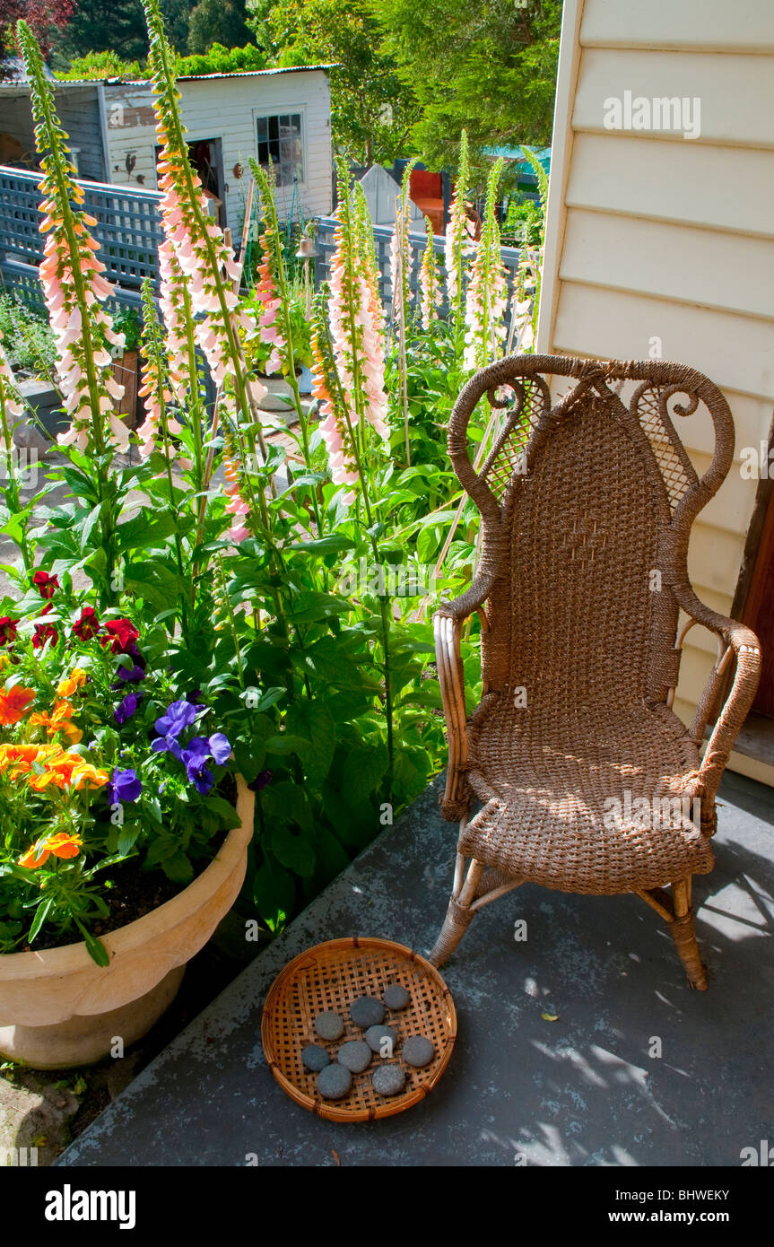 Zuckerrohr-Stuhl auf Veranda mit Stockrosen Stockfoto