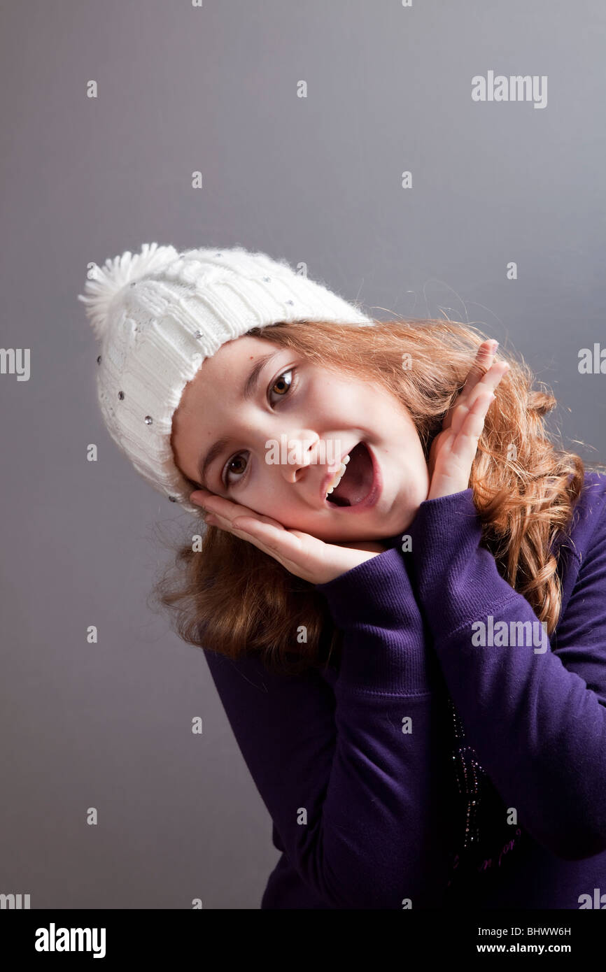 Glückliches kleines Mädchen posiert mit einem weißen Wollmütze auf dem Kopf Stockfoto