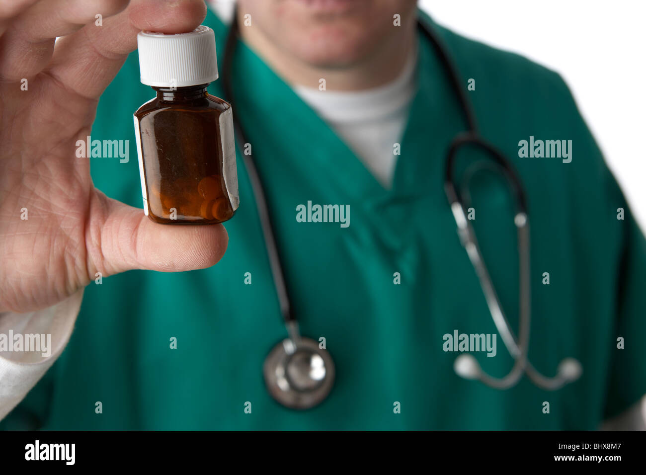Mann trägt medizinische Peelings und Stethoskop holding und mit Blick auf eine kleine Flasche Pillen Stockfoto