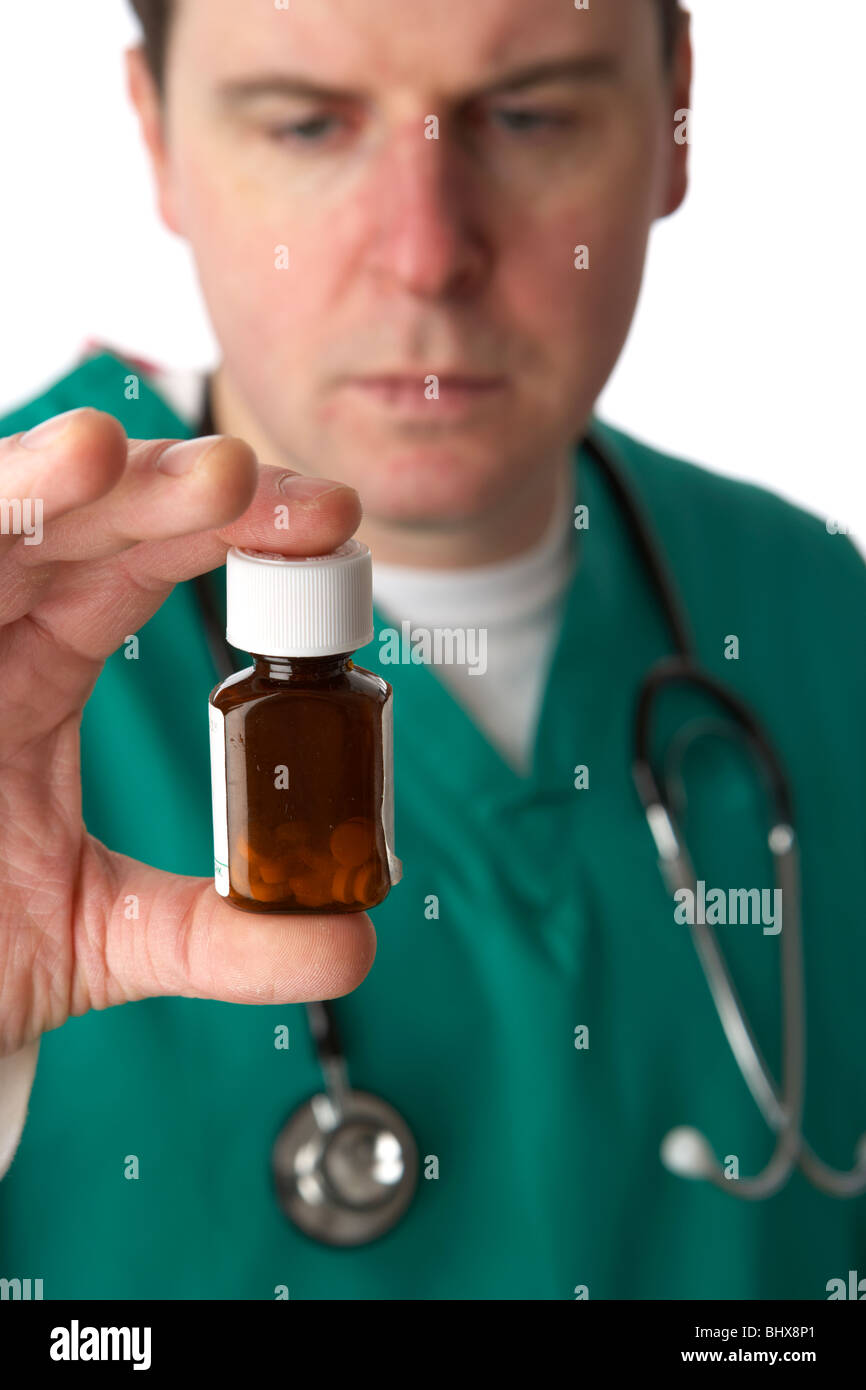 Mann trägt medizinische Peelings und Stethoskop holding und mit Blick auf eine kleine Flasche Pillen Stockfoto