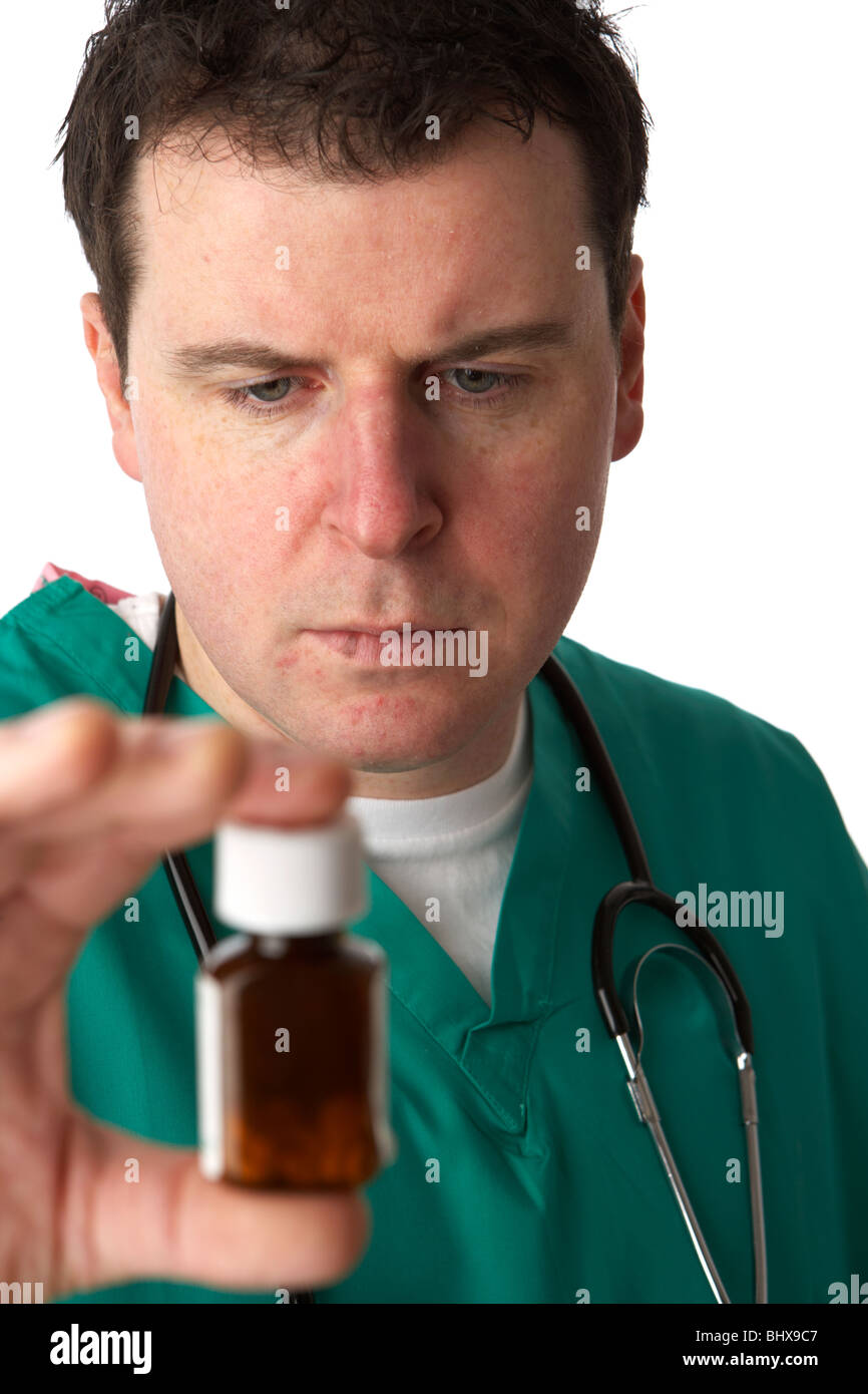 Mann trägt medizinische Peelings und Stethoskop holding und mit Blick auf eine kleine Flasche Pillen Stockfoto