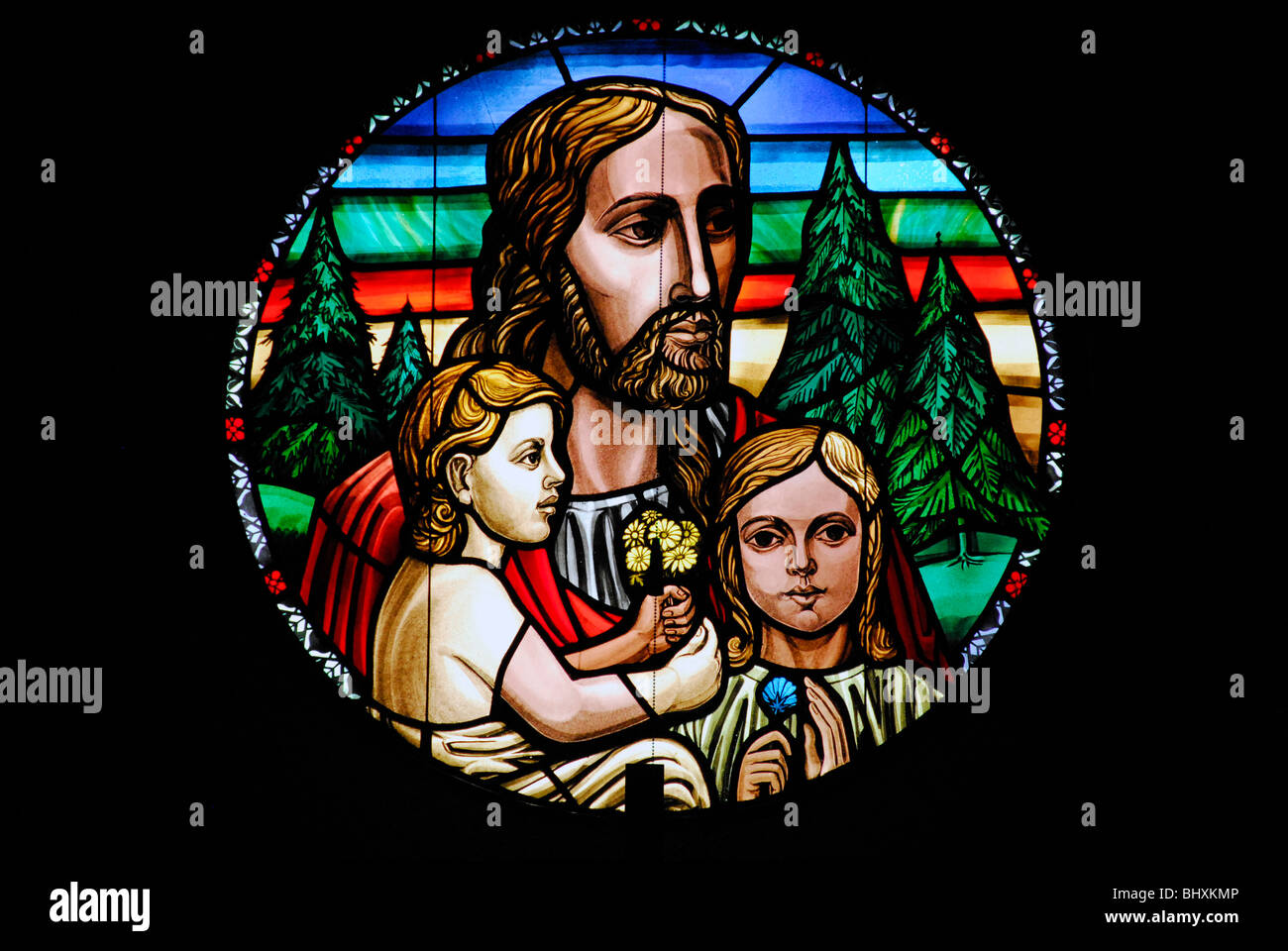 Eine kreisförmige Glasmalerei Bild von Jesus und zwei Kindern sitzt neben ihm hält Blumen. Stockfoto