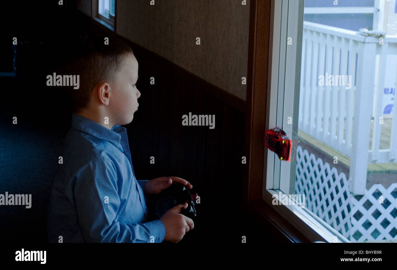 Dieses dramatische Bild zeigt einen 5 Jahre alten junge mit ein ferngesteuertes Auto auf ein Fenster in einem abgedunkelten Raum zu spielen. Stockfoto