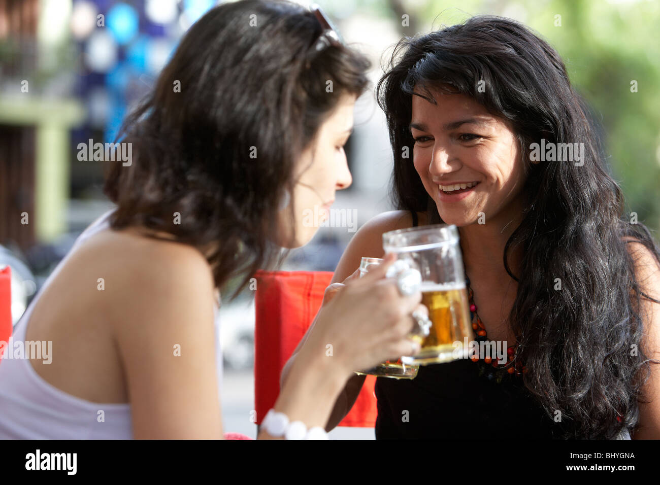 Mitte der zwanziger Jahre hispanischen Frauen teilen einen Drink und genießen ein Lachen auf Outdoor-Straße Café-Tisch Stockfoto