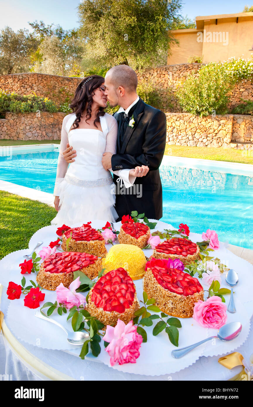 Braut und Bräutigam küssen am Tag der Hochzeit in der Nähe von Pool und Hochzeitstorten Stockfoto