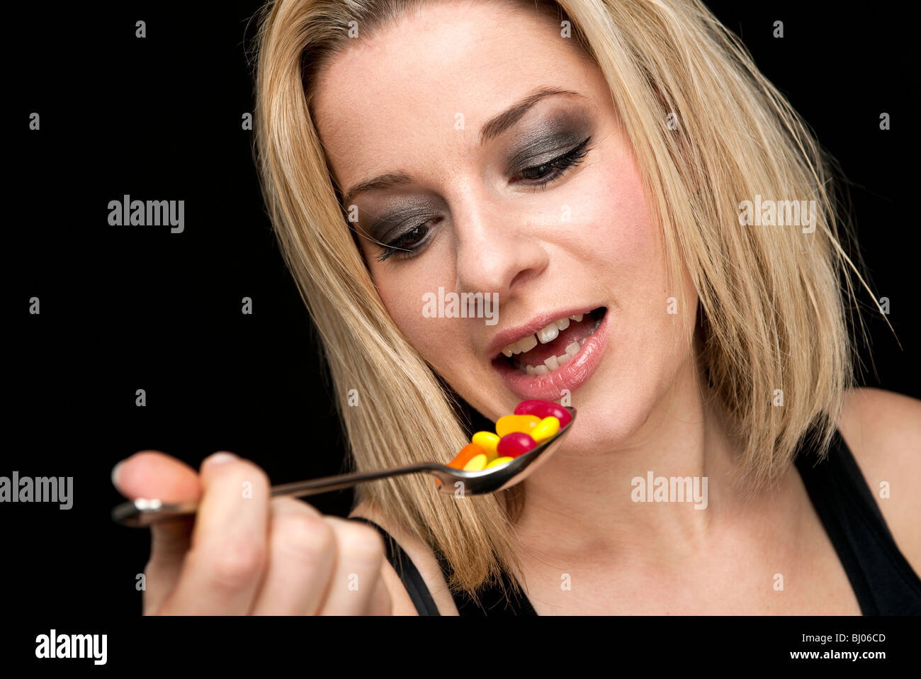 blonde Frau, die einen Löffel von Pillen oder Süßigkeiten Stockfoto