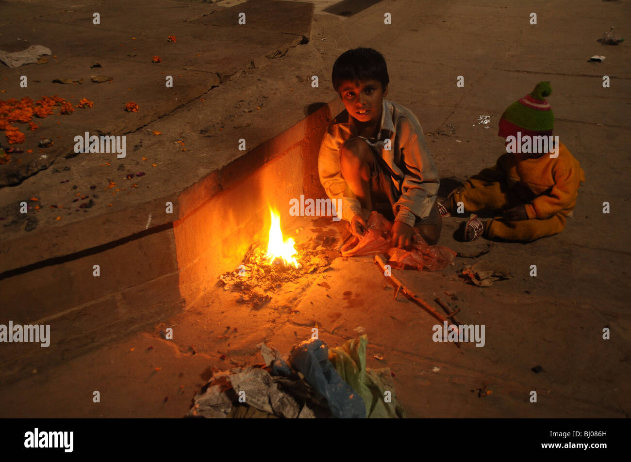 Zwei kleine Kinder leicht Feuer aus Plastiktüten zum Warmhalten auf einem des Ghats von Varanasi in Indien Stockfoto