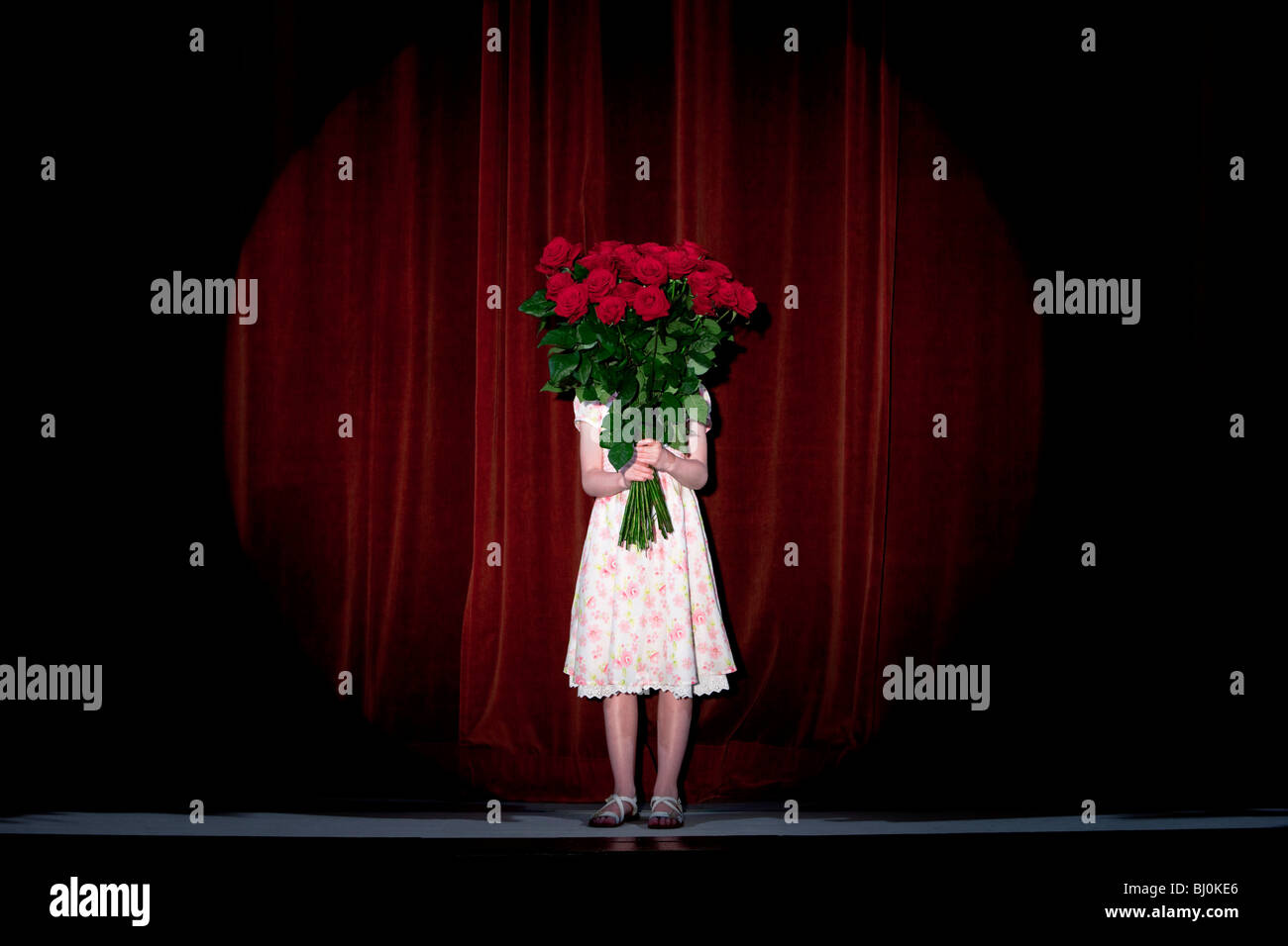 junge Mädchen stehen auf der Bühne versteckt sich hinter Strauß roter Rosen Stockfoto