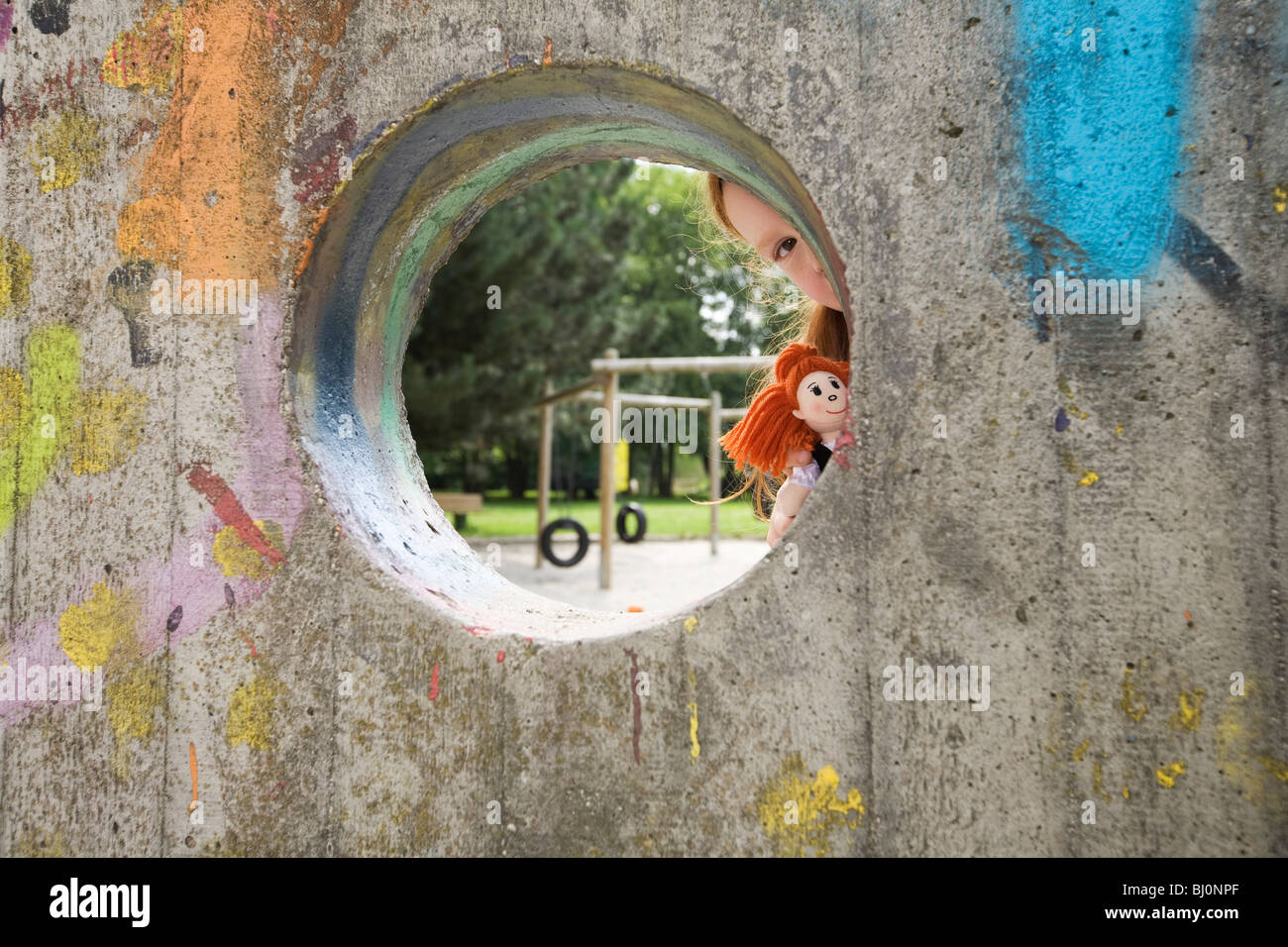 junges Mädchen spähen durch Loch in Wand auf Spielplatz Stockfoto