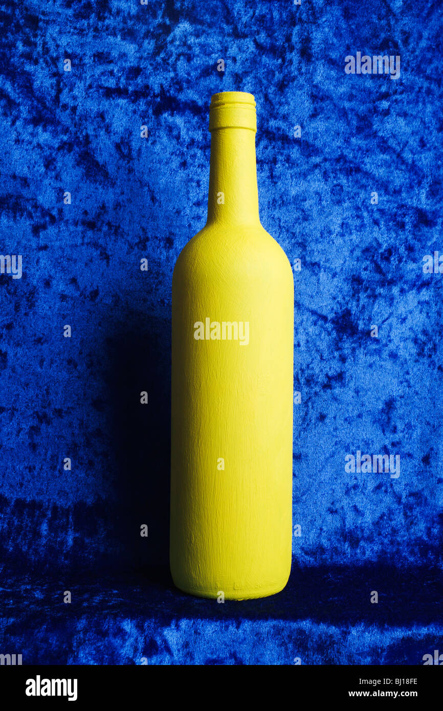 Eine gelb lackierte Flasche auf einem blauen Hintergrund. Stockfoto