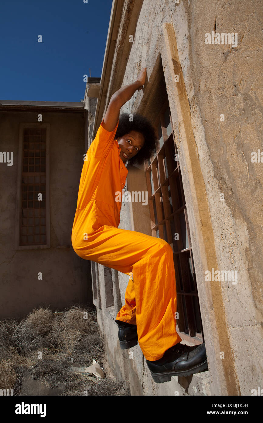 Ein afroamerikanischer Mann im orangefarbenen Gefängnis Overalls entkommt aus dem Gefängnis durch eine Kletterwand Stockfoto