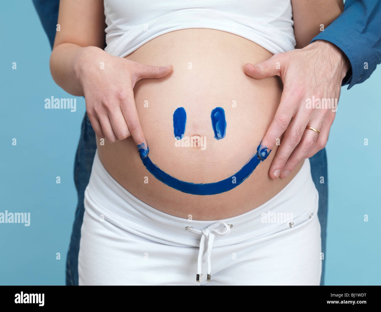Lizenz erhältlich unter MaximImages.com - schwangere junge Frau und ihr Mann malen ein fröhliches Smiley Gesicht auf ihren Bauch. Stockfoto