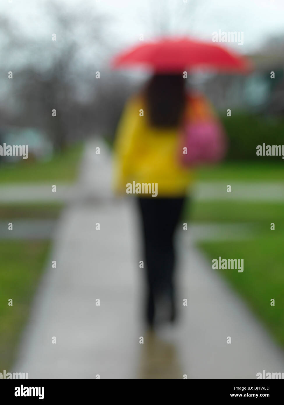 Junge Frau mit einem Regenschirm zu Fuß entlang der Straße an einem regnerischen Tag Stockfoto Junge Frau mit einem Regenschirm zu Fuß entlang der Straße an einem regnerischen Tag Stockfoto