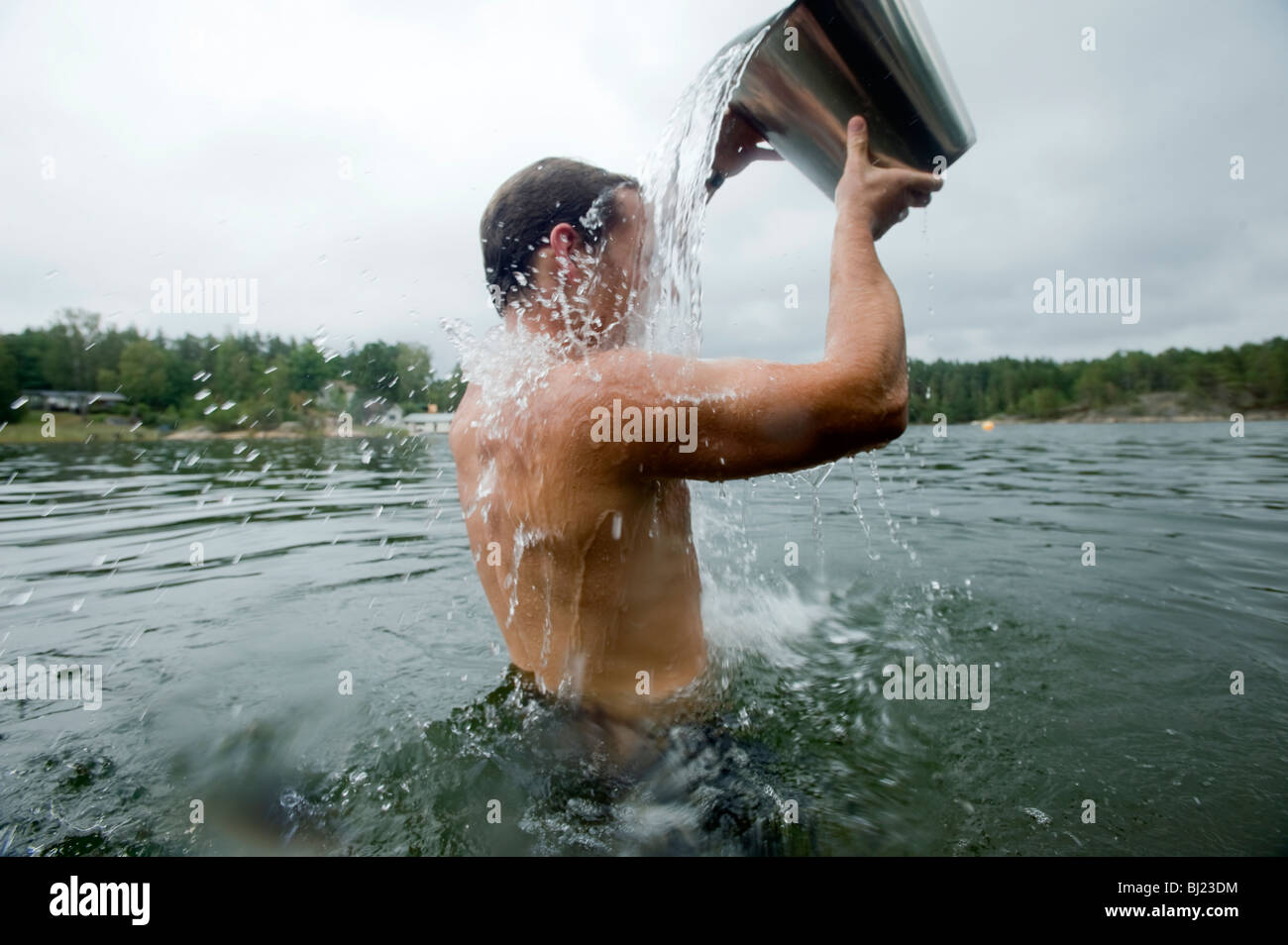 Mann im Wasser gießt Wasser über sich selbst aus einem Eimer, Schweden. Stockfoto