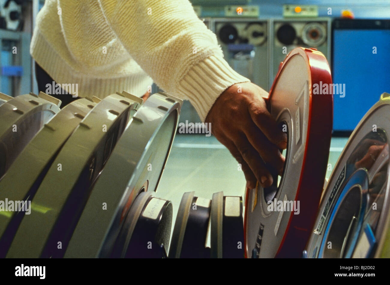1970er Jahre COMPUTERRAUM FIRMENFIRMA BANDROLLENBEDIENER HAND 1970er Jahre Firmengeschäft Hauptrahmen Büro Computerraum mit Computerbediener reicht nach Computerrollenband Stockfoto