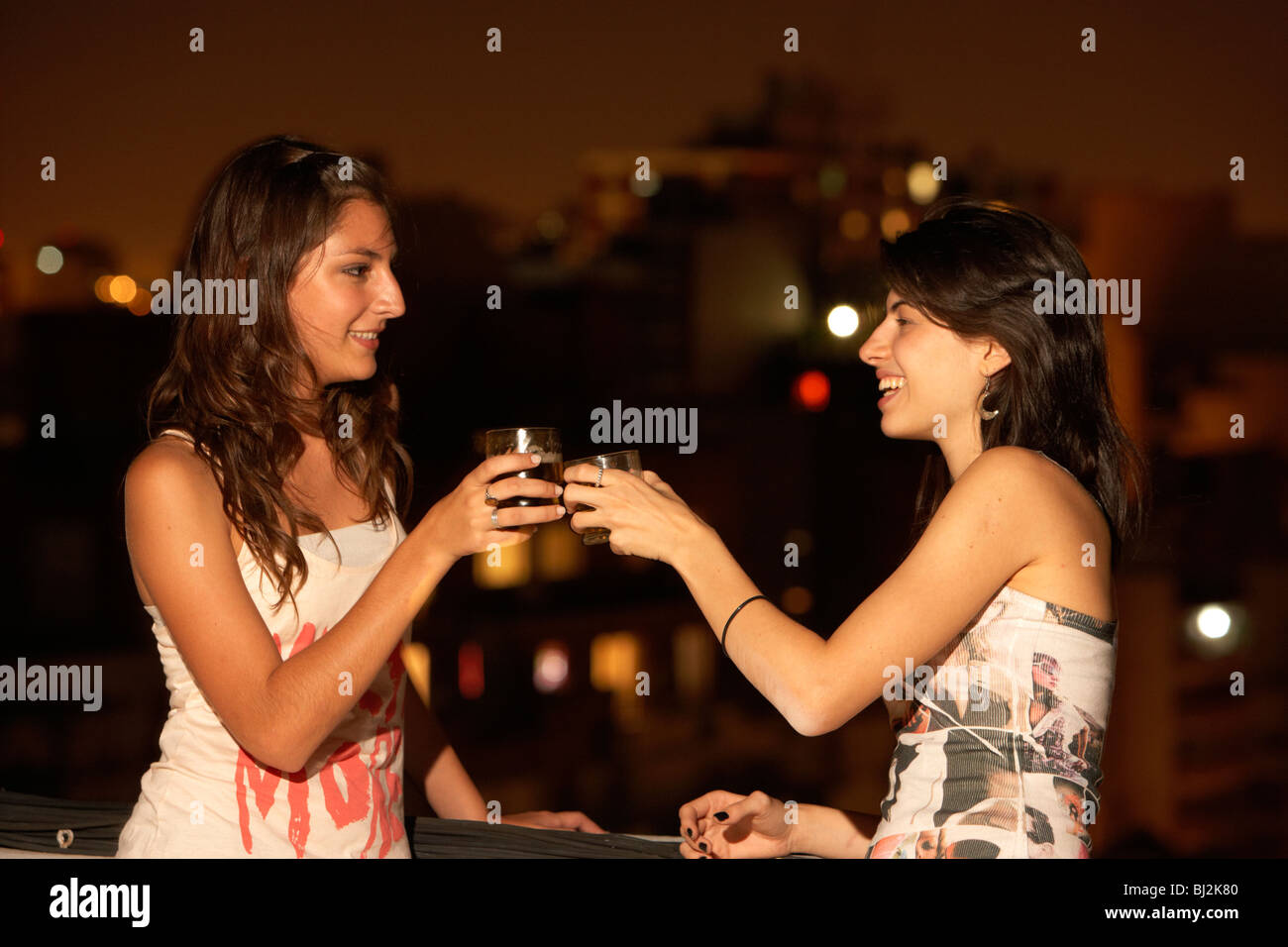 zwei junge hispanisches Latein Frauen Bier trinken und berühren Gläser zusammen auf einem Balkon party in Buenos Aires Argentinien Stockfoto