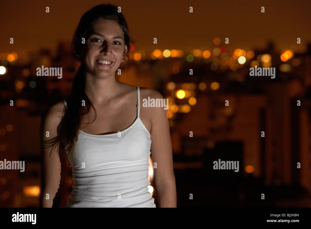 junge spanische Latin Frau stand lächelnd auf Dach mit Abend-Stadt im Hintergrund in Buenos Aires Argentinien Stockfoto