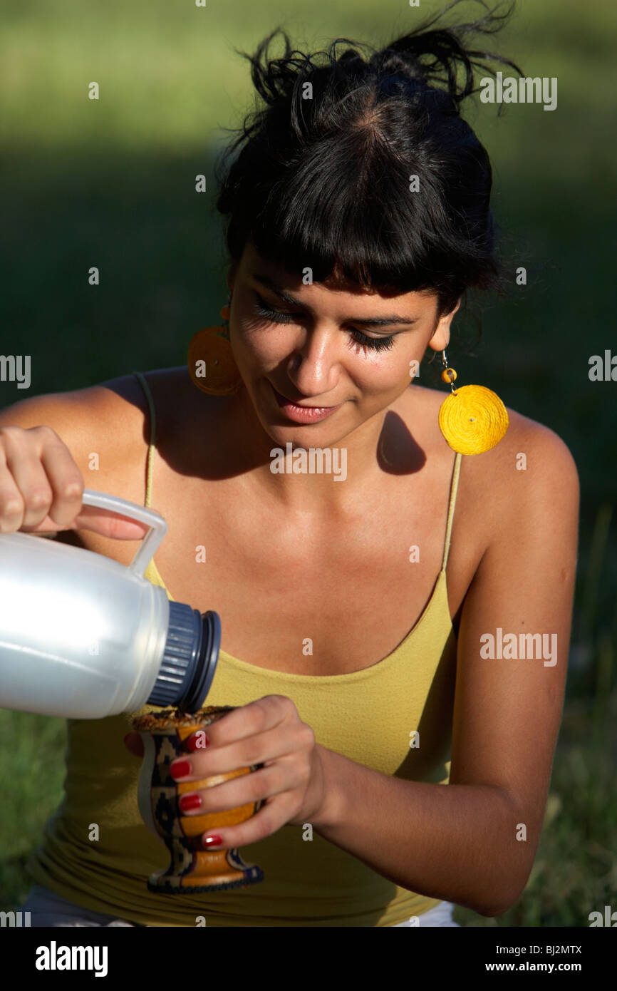 junge spanische Latin Frau gießt heißes Wasser aus einer Thermoskanne in einem Mate-Kürbis im Park in Buenos Aires Argentinien Stockfoto