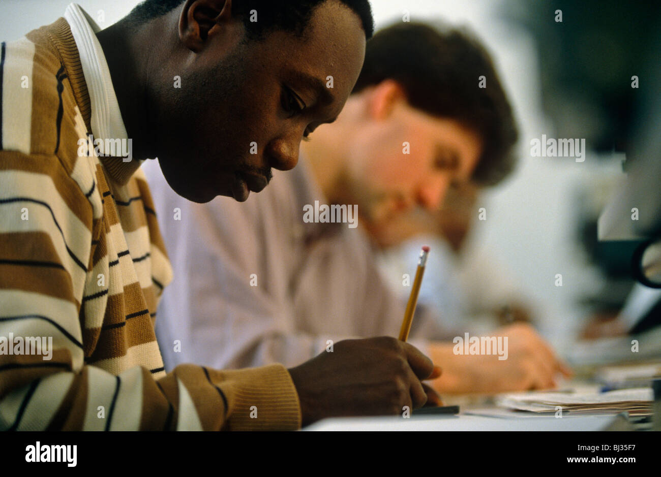 Ein Afro-Karibischen Student arbeitet fleißig neben eine hellhäutige Mann bei einem Kommunikationsunternehmen in London. Stockfoto