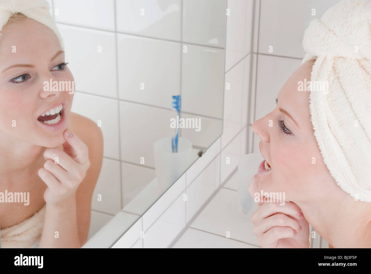 Frau mit Badetuch und Handtuch auf dem Kopf vor dem Spiegel im Badezimmer Stockfoto