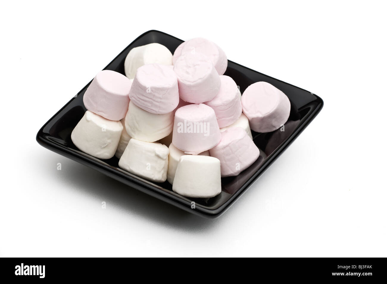 Schwarze quadratische Keramikplatte gefüllt mit rosa und weißen Marshmallows auf weißem Hintergrund Stockfoto