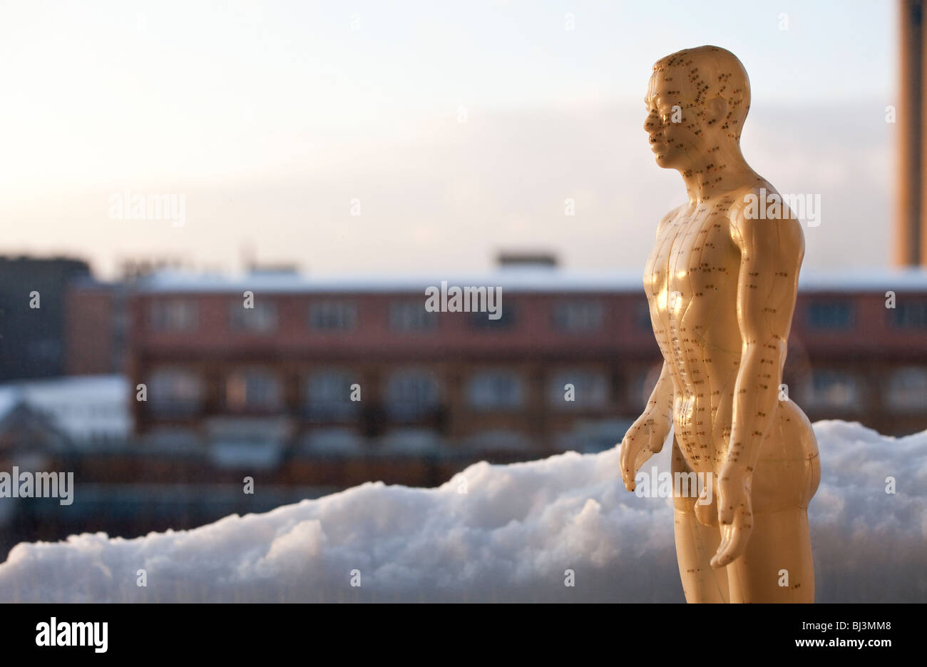 Akupunktur-Figur in den Schnee vor alten Industriegebäude, Halbfigur in der Abenddämmerung Stockfoto